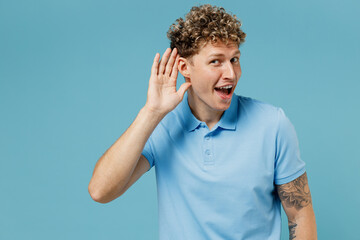 Curious nosy fun vivid energetic young curly man 20s years old wears azure t-shirt try to hear you overhear listening intently hot news isolated on plain pastel light blue background studio portrait.