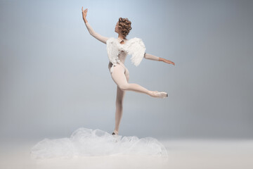 Obraz premium Full-length portrait of beautiful graceful ballerina dancing in image of angel with wings isolated on gray studio background. Art, motion, action, flexibility, inspiration concept.