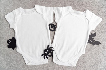 White baby rompers and spooky black paper decorations on grey soft fabric surface view from above....