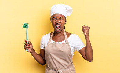 black afro chef woman shouting aggressively with an angry expression or with fists clenched...