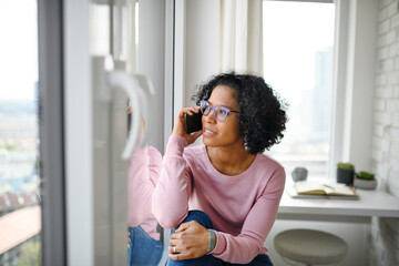 Portrait of happy mature woman making a phone call indoors, looking out of window.