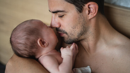 Close up of father holding and kissing his newborn baby indoors at home
