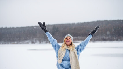 Front view portrait of senior woman outdoors standing in snowy nature, stretching arms.