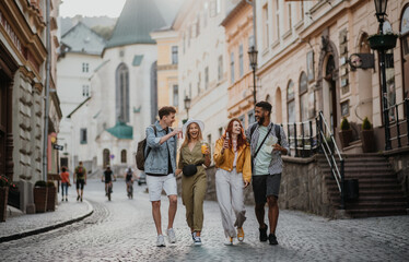 Front view of group of happy young people with drinks outdoors on street on town trip, laughing.