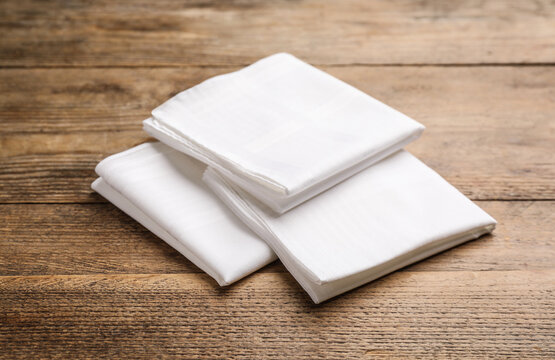 Three white handkerchiefs folded on wooden table