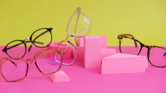 multiple eyeglasses on a pink ang yellow background, geometric stands, trendy eyeglass frames rolling geometric podiums