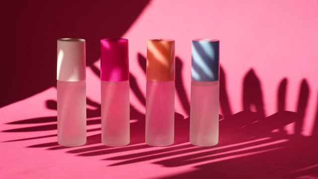 shade from a swaying palm leaf on several spray glass bottles with perfume on pink geometric podiums, composition for perfume presentation, four perfume bottles on stage, pink background