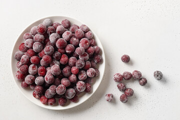 Frozen red sour cherry in white plate on a white background. View from above.