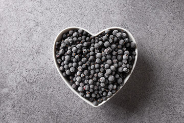 Frozen black currant in plate shaped as heart isolated on a gray background. View from above. Concept love eco organic food.
