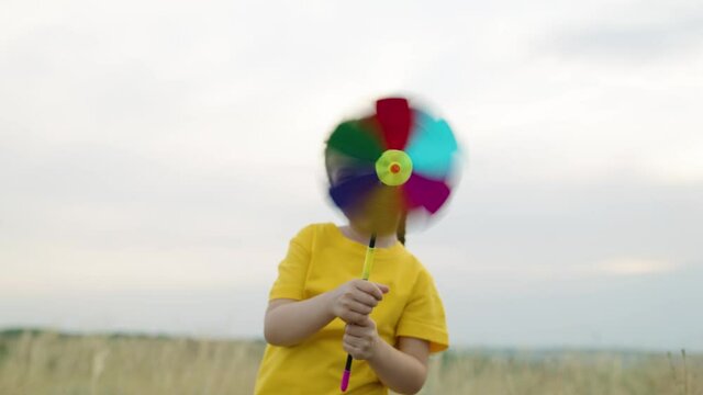 little girl plays with a toy multicolored turntable in her hand in autumn in park. Happy child kid playing fun windmill turntable outdoors. Happy family resting on a weekend in nature. Family holiday