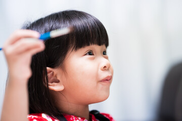 Closeup adorable child face sweet smile. Asian girl holding paintbrush. Happy learning concept.