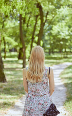 Fototapeta na wymiar Beautiful blonde girl in a dress with flowers, rear view. Photo of a young girl in the park. 