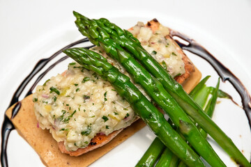 Baked Salmon with Cheese Gratin Garnished with Asparagus and Cherry Tomatoes on a White Plate
