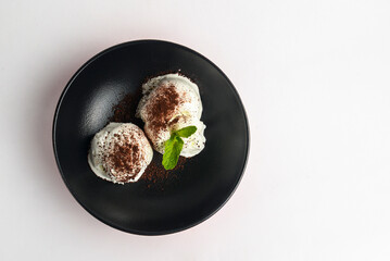 Vanilla ice-cream scoops in a black bowl over white background. White ice cream with cocoa powder and fresh mint on top.