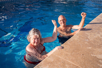 Old couple raising fists up while swimming in pool