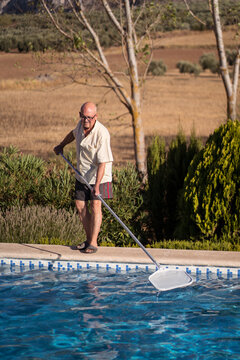 Old man cleaning swimming pool in backyard