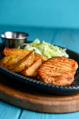 Grilled Chicken Steak with fried potatoes in rural style and coleslaw salad served in a tray over blue background.