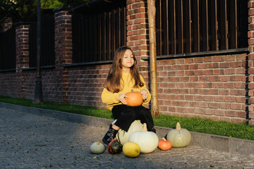 Funny child girl in orange pullover for Halloween with pumpkin and on a dark brick background.