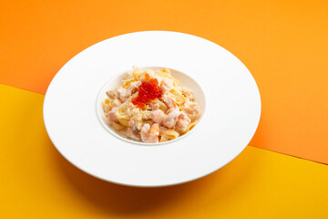 Pasta with seafood and red caviar. In a plate on a colored background.