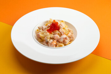 Pasta with seafood and red caviar. In a plate on a colored background.
