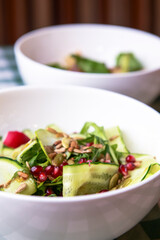 Spinach salad with tomatoes, fresh arugula, pumpkin seeds, pomegranate seeds served in a white bowl