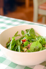 Spinach salad with tomatoes, fresh arugula, pumpkin seeds, pomegranate seeds served in a white bowl