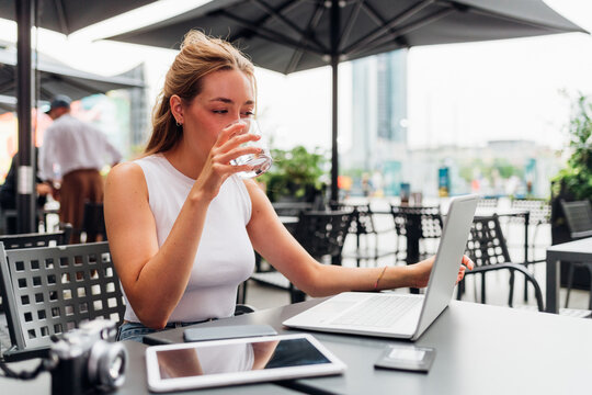 Young flexible worker business woman remote working sitting bar drinking water
