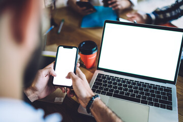 Unrecognizable man using smartphone and laptop at table with colleagues