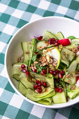 A large dish with a grilled zucchini salad with fresh cucumbers, radish, pomegranate seeds and fresh arugula.