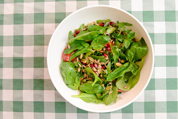 Spinach salad with tomatoes, fresh arugula, pumpkin seeds, pomegranate seeds served in a white bowl