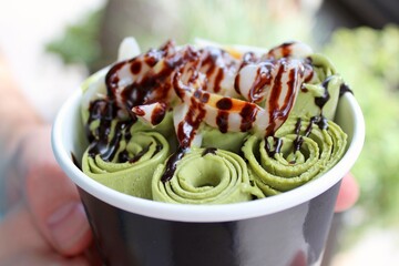 A bowl of sweet stir-fried ice cream, also known as rolled ice cream, a Thai frozen dessert with sugar, matcha, litchi and chocolate sauce, an exotic food and a popular treat.