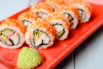 California sushi rolls served on a red plate over light wooden background. Close up, selective focus on sushi.