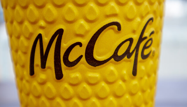 Paper yellow glass glass with coffee for McCafe drinks on the table against blurred city from McDonald's. Fast food business background. Fast food restaurant menu. Ukraine, Kiev - September 13, 2021.