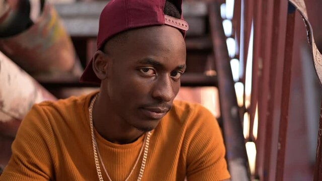 The camera zooms in on a young black guy sitting on a staircase in an alley in a dysfunctional neighborhood. Ghetto and young man