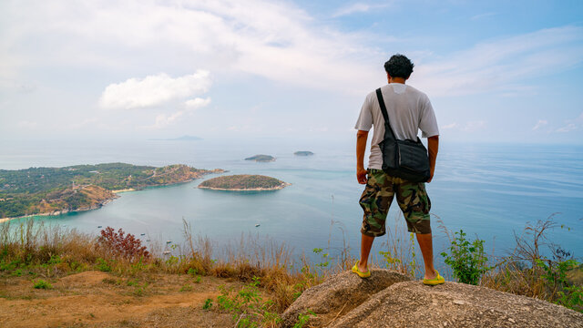 Travel man photographer standing on rock to see landscape view at Phahindum viewpoint popular landmark in Phuket Thailand Viewpoint to see promthep cape Naiharn beach and yanui beach Amazing view