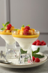 Delicious panna cotta with mango and raspberries on grey table