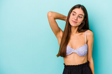 Young caucasian woman wearing bikini isolated on blue background touching back of head, thinking and making a choice.
