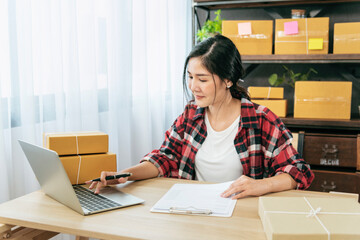 Woman checking stock goods supply delivery package shipping use document checklist. Asian woman startup small business at home office. Online entrepreneur asian woman use tablet checking online order