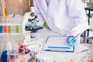 Fototapeta premium Closeup Woman scientist hand use dropper in lab look at science microscope medical test, research biology chemistry. Females technician laboratory analyzing blood scientific pharmaceutical research.