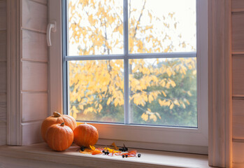 Orange pumpkins on windowsill, candles, autumn leaves, lantern.