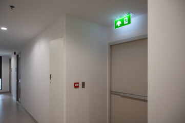 Green fire exit sign over the exit door in the building. - obrazy, fototapety, plakaty