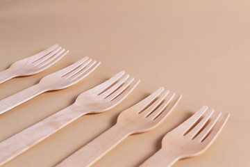 Wooden forks lie in a row on a cream background. Rhythm. Eco friendly stuff concept. Horizontal orientation. Copy space.
