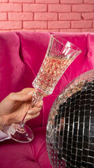 woman holding a glass of champagne on pink background with crystal ball