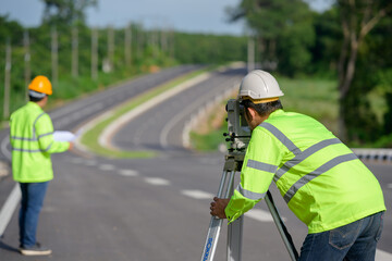 Picture of two civil engineers using theodolites measuring land coordinates standing at outdoor theodolites at a road construction site.