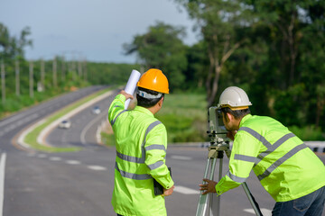 Picture of two civil engineers using theodolites measuring land coordinates standing at outdoor...