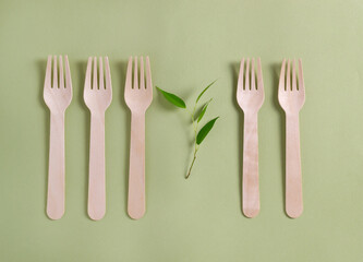 Five bamboo wood forks with a plant lie in a row on a green background. No plastic concept. Top view.