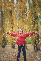 Girl playing with the fallen autumn leaves on a walk in the forest