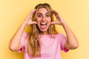 Young caucasian blonde woman isolated on yellow background  receiving a pleasant surprise, excited and raising hands.