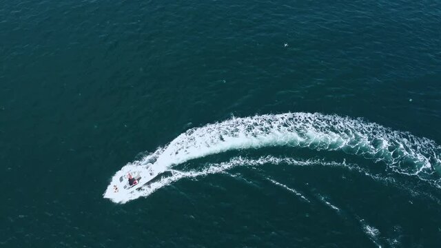Aerial view of a speedboat moving in a circle for a turn, with a man and two girls on board