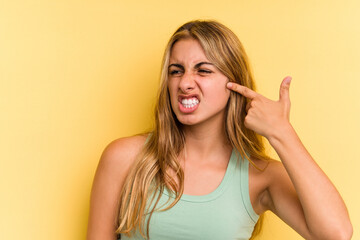 Young caucasian blonde woman isolated on yellow background  covering ears with hands.